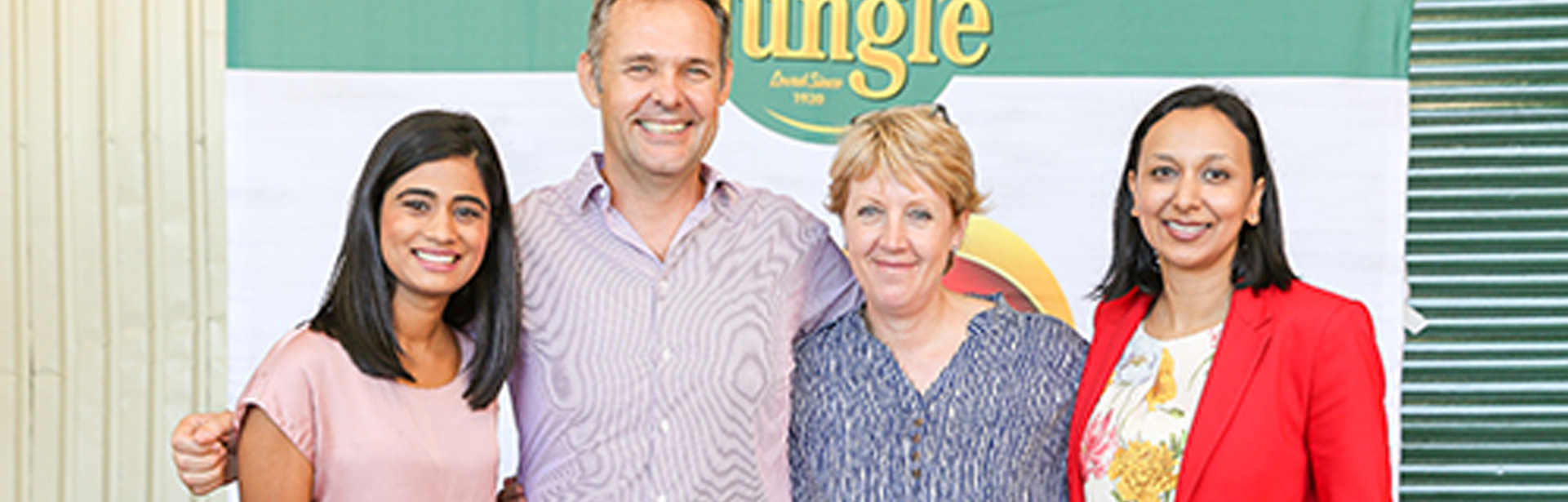 A group of diverse people standing together, smiling behind a background